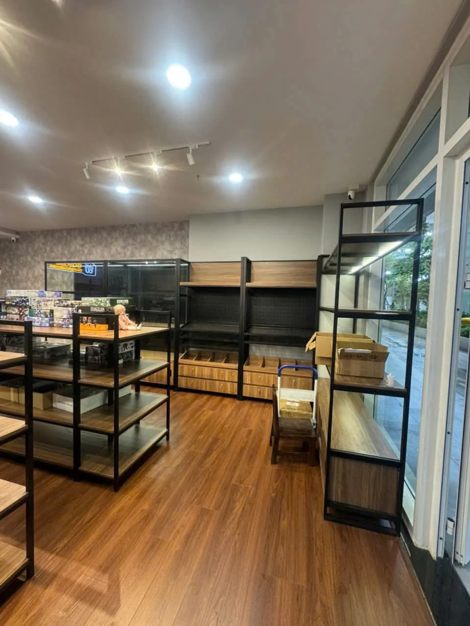 Kệ trưng bày khung sắt sơn tĩnh điện và mặt gỗ đặt dọc cửa kính shop mô hình