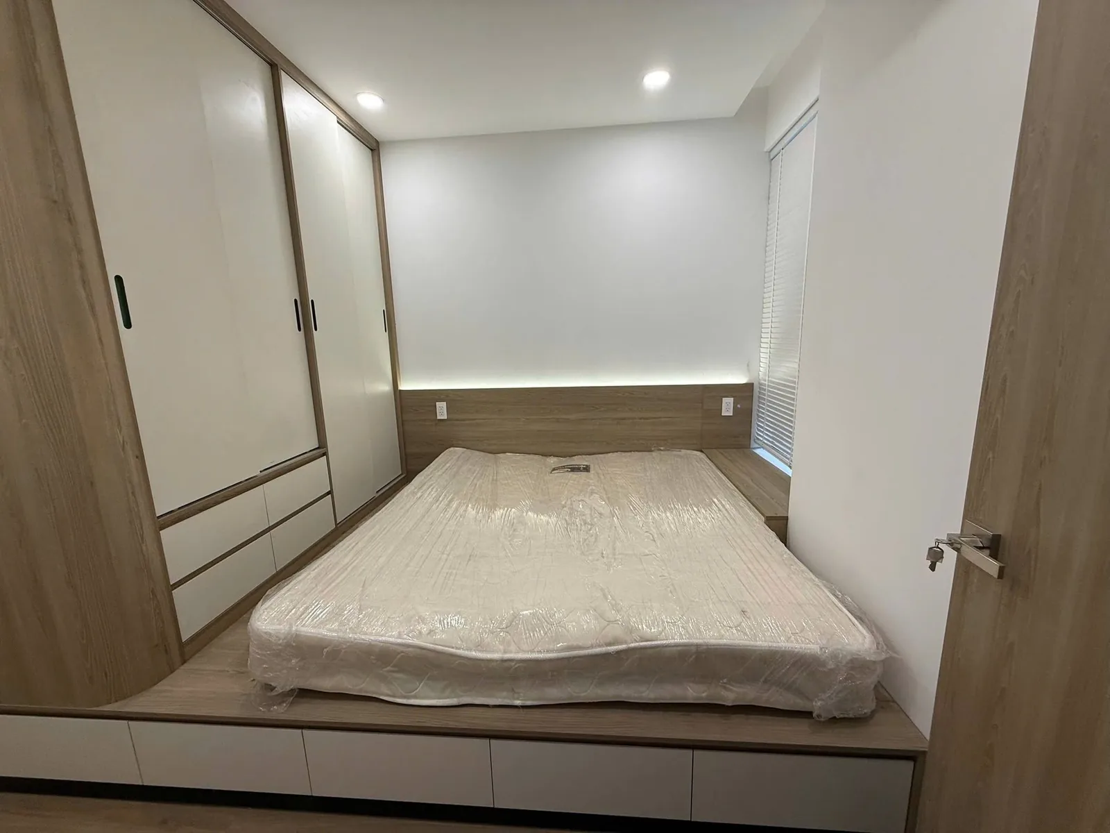 Phòng ngủ master nội thất gỗ Phòng ngủ master căn hộ Eastmark City với giường bục, tủ áo kịch trần và LED đầu giường